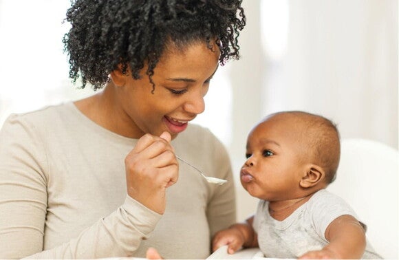 woman spoon feeding baby sitting in high chair